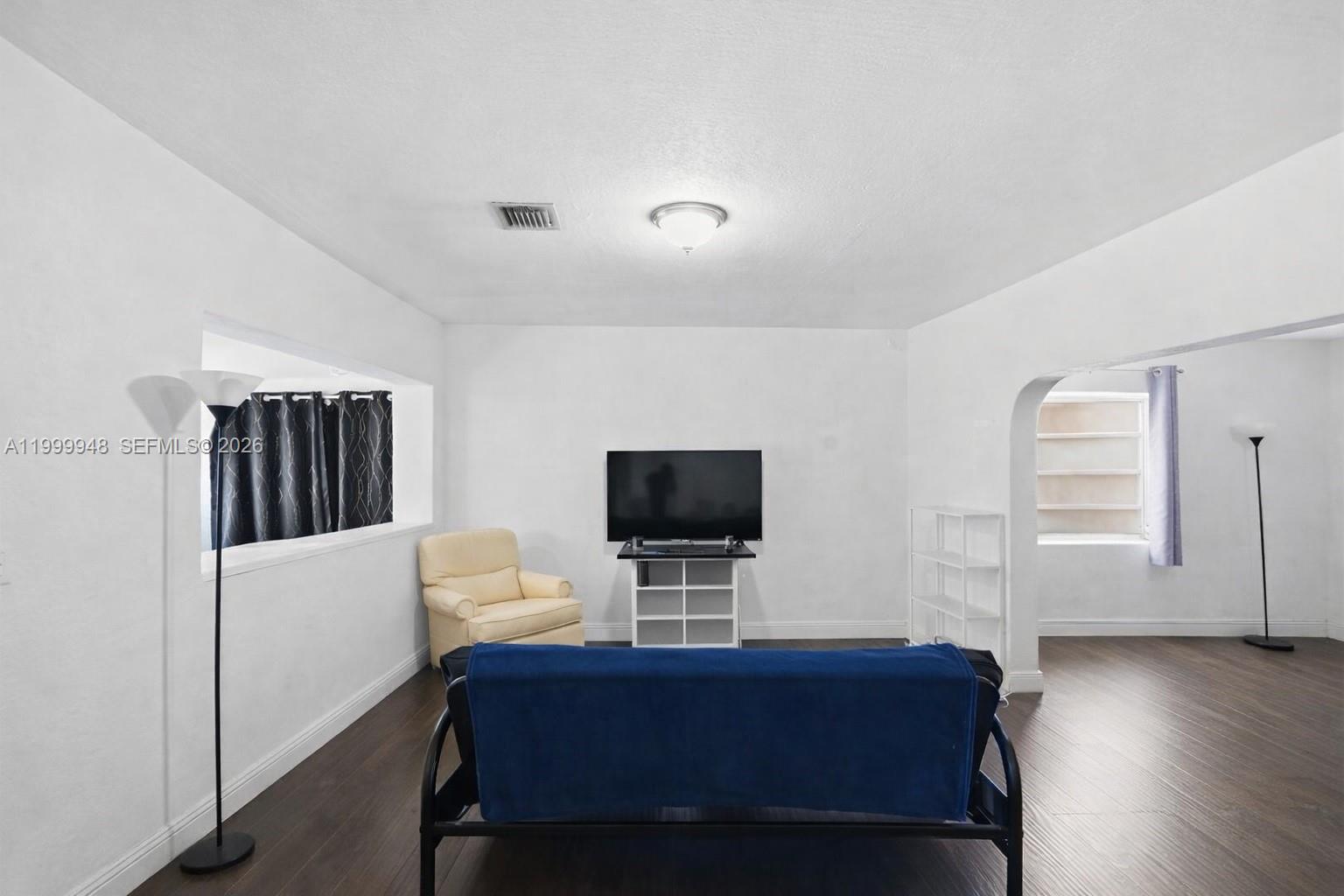 A living room features dark wood-look flooring, white walls, a television, and a blue sofa — 3645 SW 25th Ter, Miami FL 33133, MIAMI, FL
