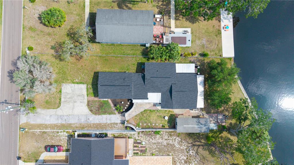 An aerial view shows a house with a dark roof situated between a road and water — 5822 RIVER ROAD, NEW PORT RICHEY, FL