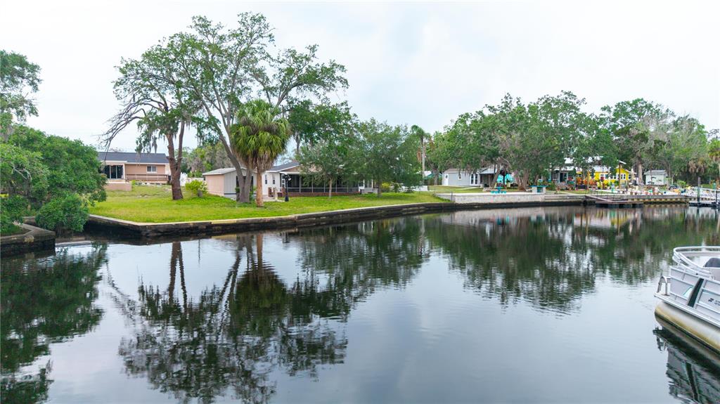 A canal-front property features a grassy lawn, mature trees, and a docked pontoon boat — 5822 RIVER ROAD, NEW PORT RICHEY, FL
