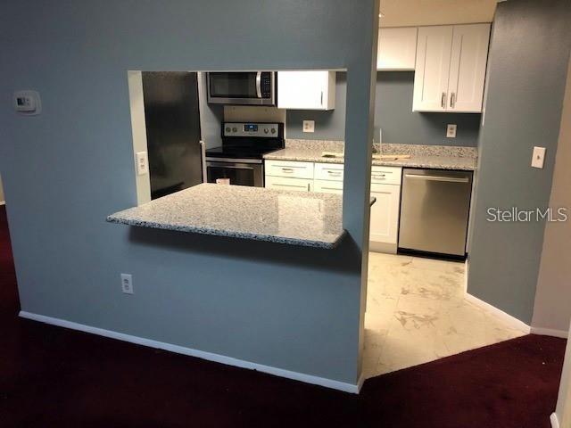 A kitchen with white cabinets, stainless steel appliances, and a granite breakfast bar — 124 LOBLOLLY COURT UNIT D, OLDSMAR, FL