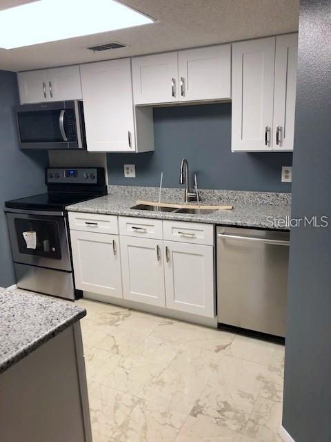 A kitchen features white cabinets, stainless steel appliances, and granite countertops against a blue wall — 124 LOBLOLLY COURT UNIT D, OLDSMAR, FL