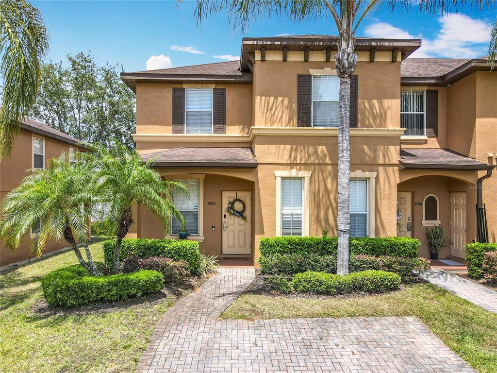 A two-story tan stucco townhouse with a brick walkway and a palm tree in front — 2744 CALABRIA AVENUE, DAVENPORT, FL