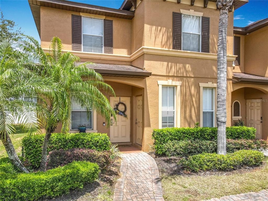 A two-story tan stucco townhouse features a brick walkway, palm trees, and manicured hedges — 2744 CALABRIA AVENUE, DAVENPORT, FL