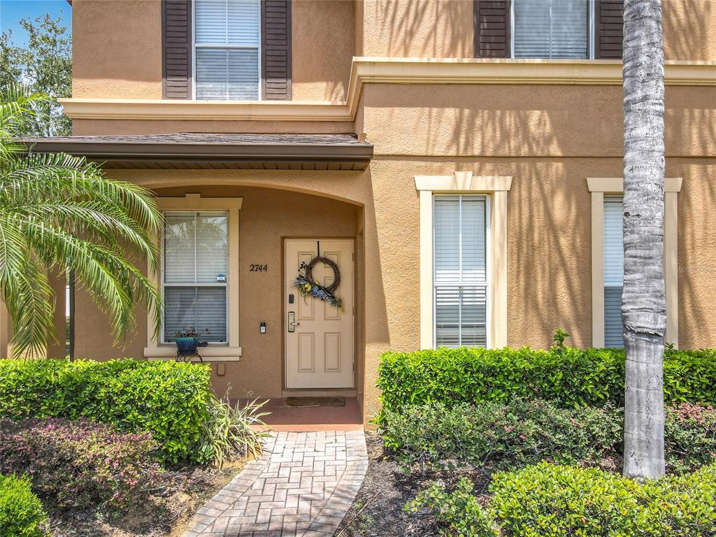 The exterior of a two-story tan house features a front door, windows, and landscaping — 2744 CALABRIA AVENUE, DAVENPORT, FL