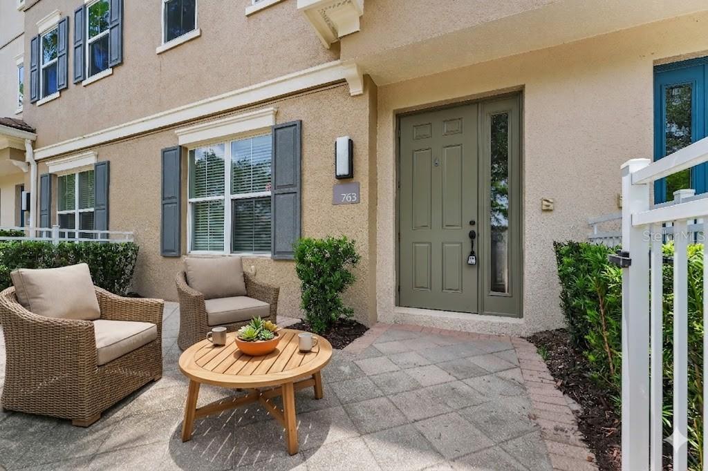A patio with two wicker chairs and a round wooden table sits before a front door — 763 GREYBULL RUN, LAKE MARY, FL