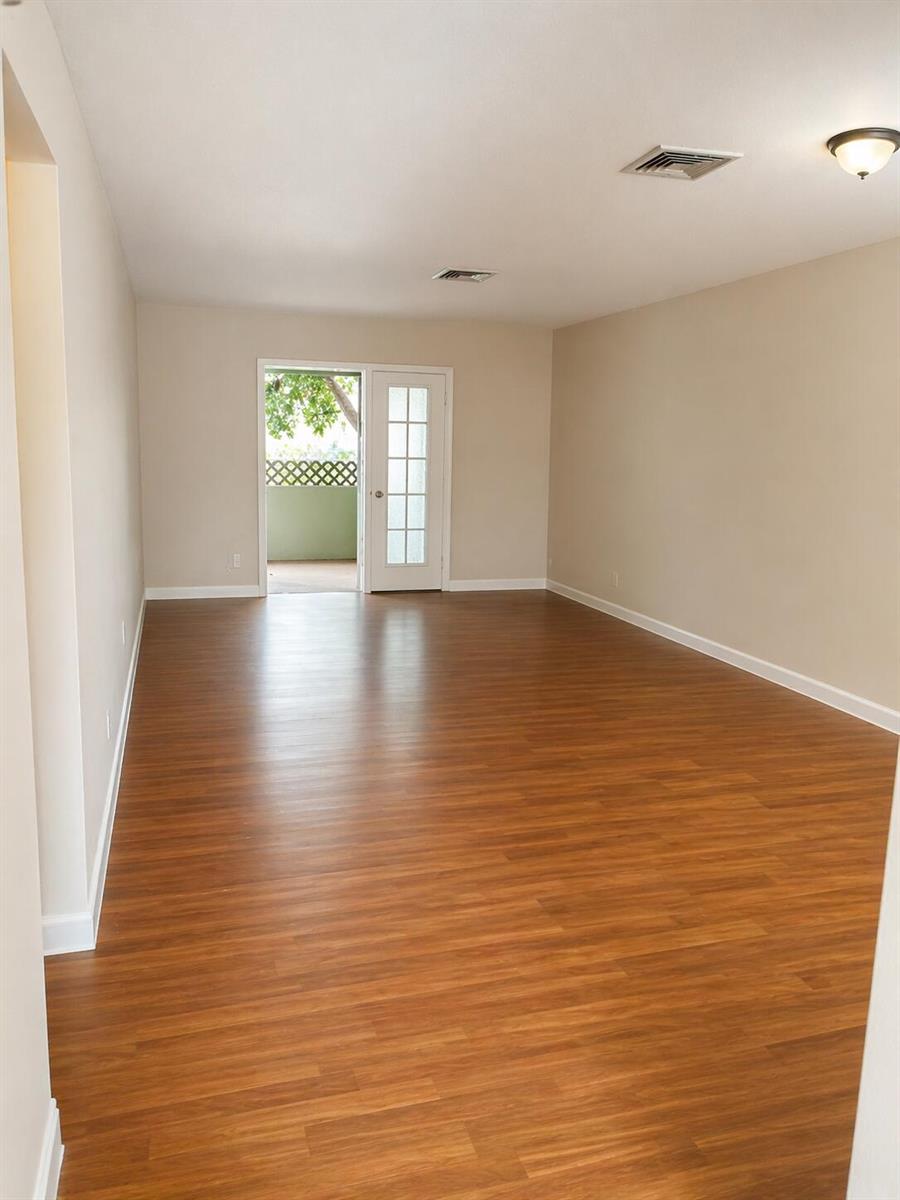 An empty room with wood-look flooring, beige walls, and a glass-paneled door leading outside — 4317 Cocoanut Road, West Palm Beach FL 33406, WEST PALM BEACH, FL