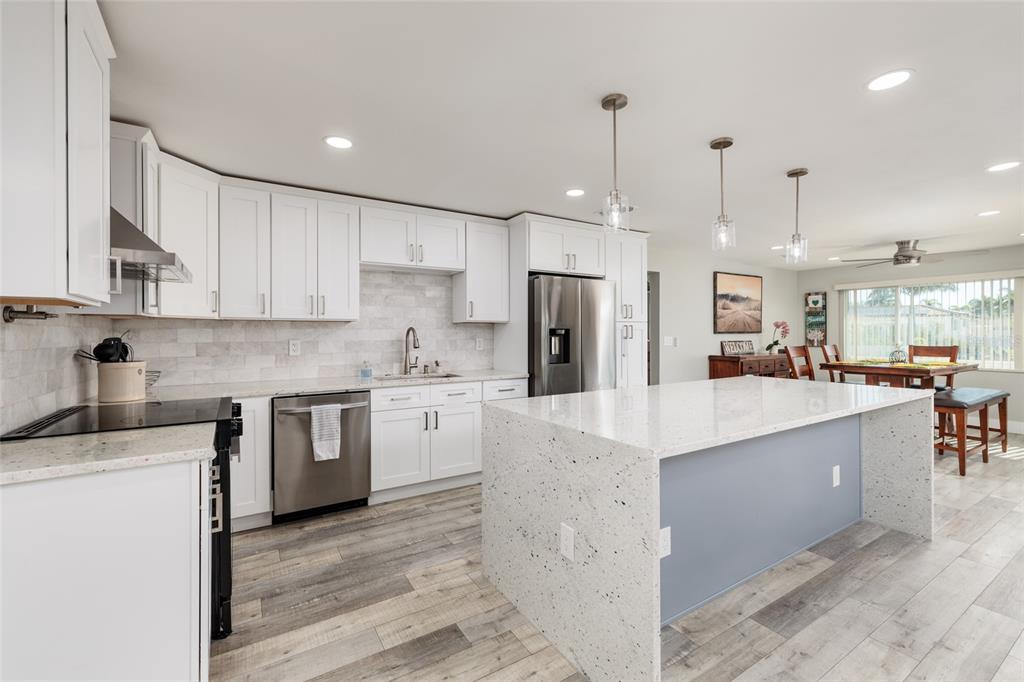A modern kitchen features white cabinets, a speckled quartz island, and light wood-look flooring — 9773 1ST STREET NE, ST PETERSBURG, FL