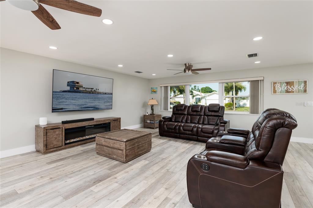 A living room features wood-look flooring, a large wall-mounted television, and brown leather seating — 9773 1ST STREET NE, ST PETERSBURG, FL
