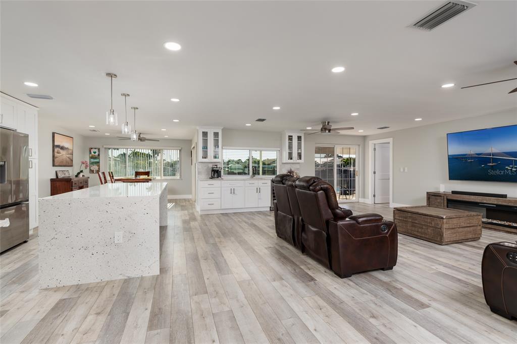 An open-concept kitchen and living area features white cabinetry, a speckled island, and wood-look flooring — 9773 1ST STREET NE, ST PETERSBURG, FL