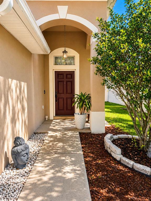 A concrete walkway leads to a brown front door under a covered arched entryway — 7942 ENDLESS SUMMER COURT, LAND O LAKES, FL