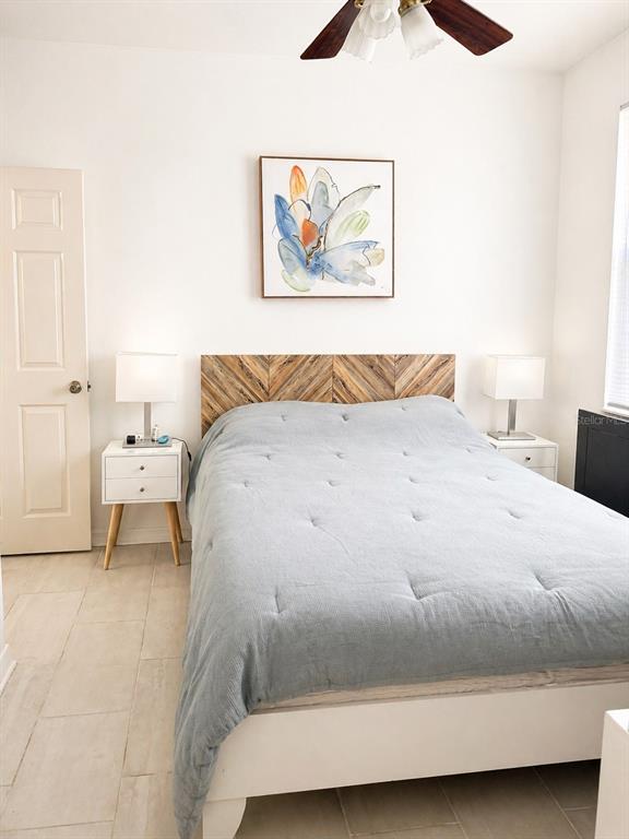 A bedroom features a bed with a chevron wood headboard, light blue bedding, and tile flooring — 7942 ENDLESS SUMMER COURT, LAND O LAKES, FL