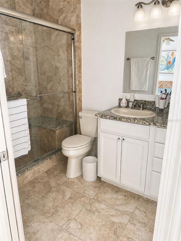 A bathroom features a tiled walk-in shower, a white vanity with granite countertop, and toilet — 7942 ENDLESS SUMMER COURT, LAND O LAKES, FL