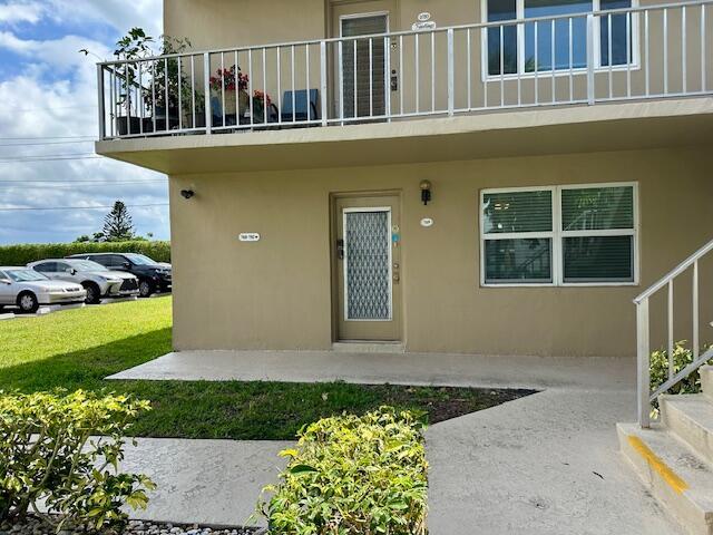 A two-story tan building features a ground-level entrance, a balcony above, and a parking area — 769 Burgundy Q, Delray Beach FL 33484, DELRAY BEACH, FL