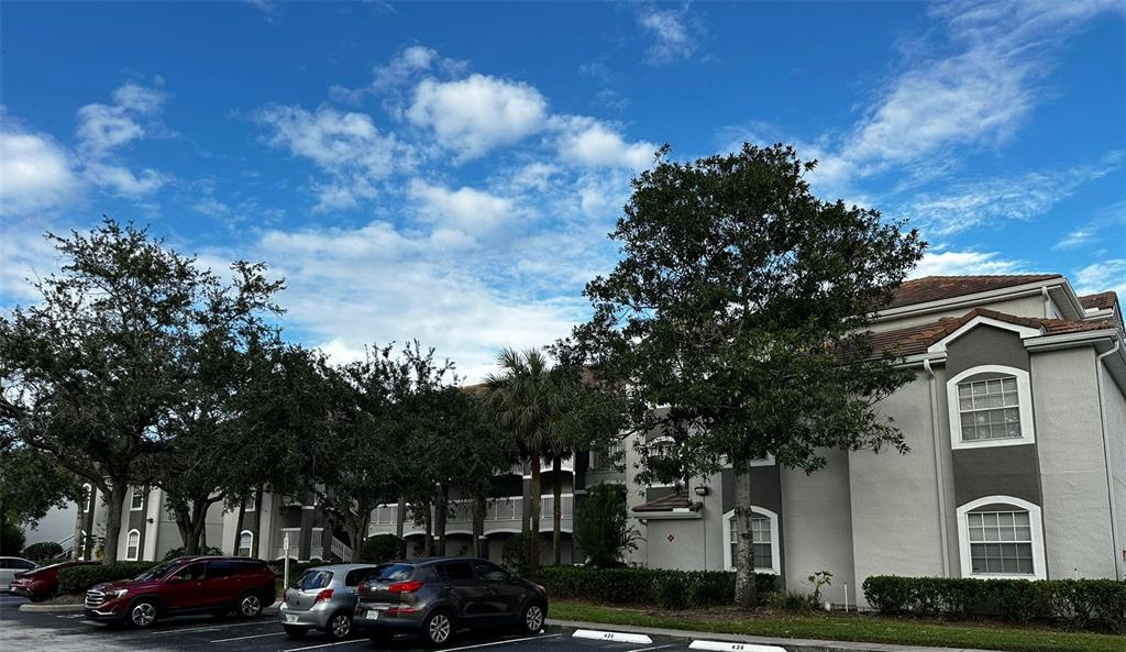A multi-story apartment building with gray siding, a tile roof, and a parking lot — 14013 FAIRWAY ISLAND DRIVE UNIT 415, ORLANDO, FL