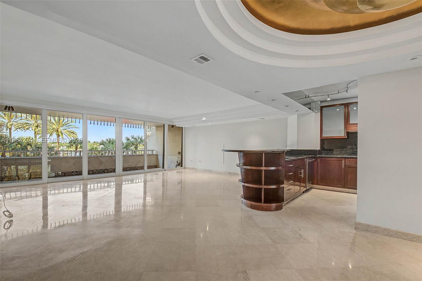 An open-concept living area features marble floors, a curved wooden bar, and floor-to-ceiling glass doors — 3 Grove Isle Dr # C208, Miami FL 33133, MIAMI, FL