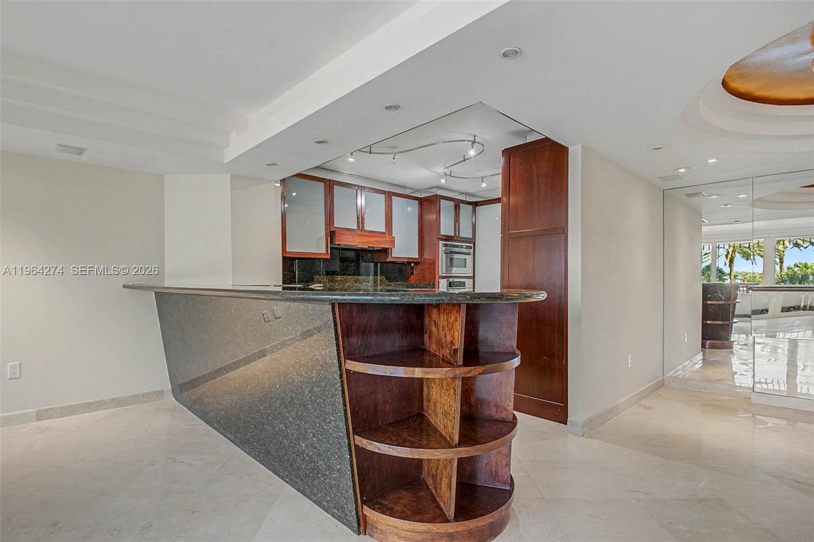 A kitchen features a dark granite breakfast bar, wood cabinetry, and light tile flooring — 3 Grove Isle Dr # C208, Miami FL 33133, MIAMI, FL