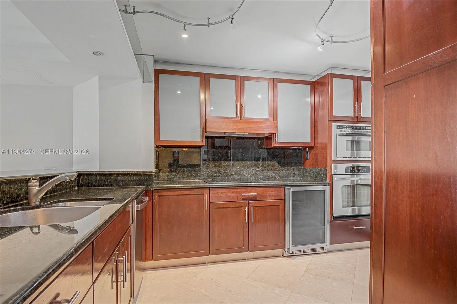 A kitchen features dark wood cabinets, granite countertops, stainless steel appliances, and tile flooring — 3 Grove Isle Dr # C208, Miami FL 33133, MIAMI, FL