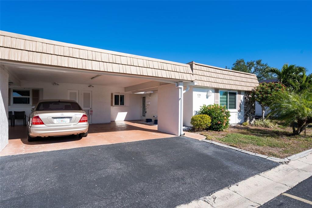 A single-story house features a covered carport, a parked sedan, and a landscaped front yard — 2305 RIVERBLUFF PARKWAY UNIT V256, SARASOTA, FL