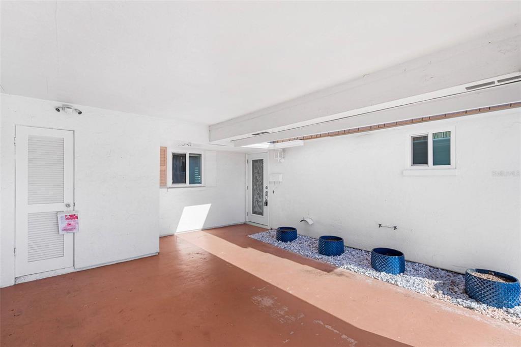 A covered patio with a red floor, white walls, and blue planters on gravel — 2305 RIVERBLUFF PARKWAY UNIT V256, SARASOTA, FL