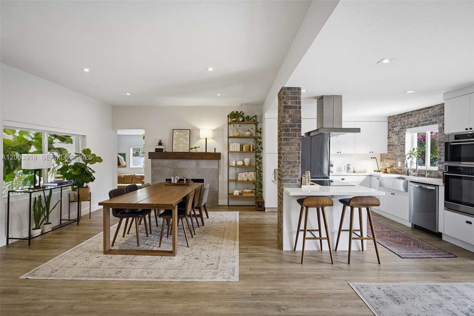 An open-concept kitchen and dining area features a brick pillar, wooden table, and white cabinetry — 565 South Dr, Miami Springs FL 33166, MIAMI SPRINGS, FL