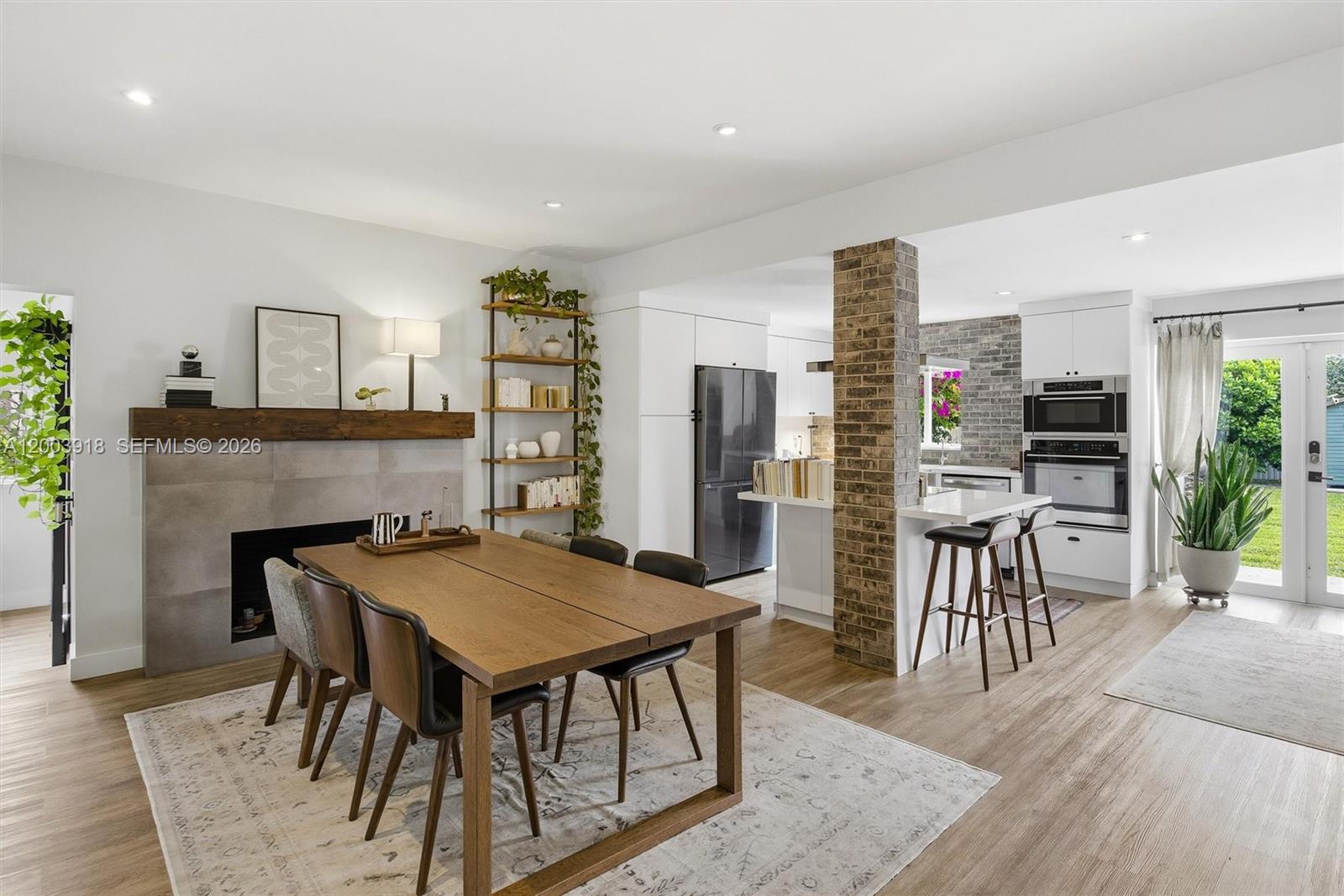 A dining area with a fireplace and wood table opens into a kitchen with brick — 565 South Dr, Miami Springs FL 33166, MIAMI SPRINGS, FL