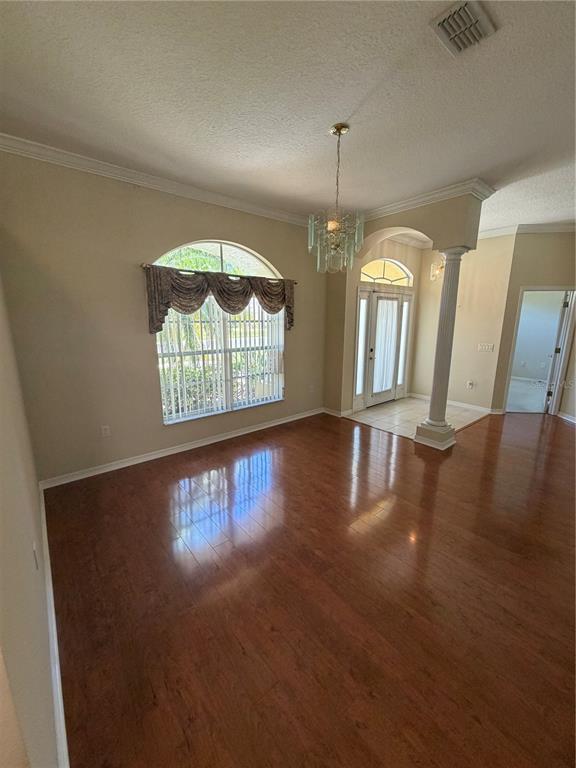 An empty dining room features hardwood floors, a chandelier, and an arched window with valances — 11855 TEE TIME CIRCLE, NEW PORT RICHEY, FL