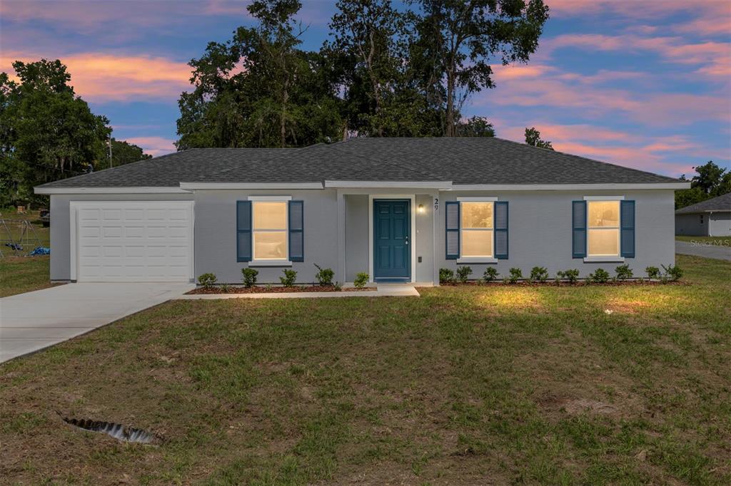 A single-story gray house with a blue front door, white garage, and dark shutters — 29 JUNIPER PASS LANE, OCALA, FL