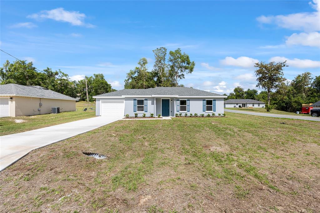 A single-story house with a light gray exterior, blue shutters, and a concrete driveway — 29 JUNIPER PASS LANE, OCALA, FL