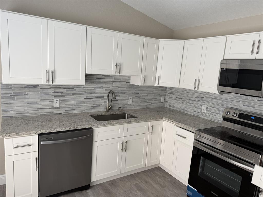 A kitchen features white cabinets, granite countertops, a stainless steel dishwasher, and a tiled backsplash — 1938 SW DUKE STREET, ARCADIA, FL