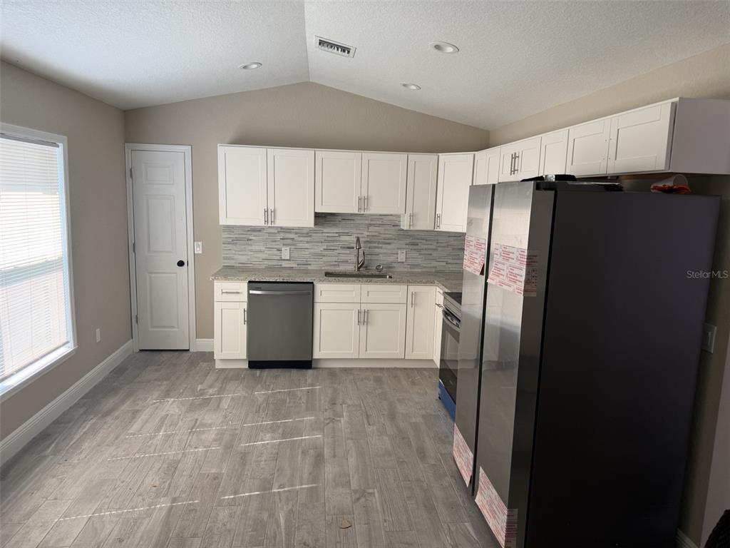A kitchen features white cabinets, stainless steel appliances, a tiled backsplash, and gray wood-look flooring — 1938 SW DUKE STREET, ARCADIA, FL