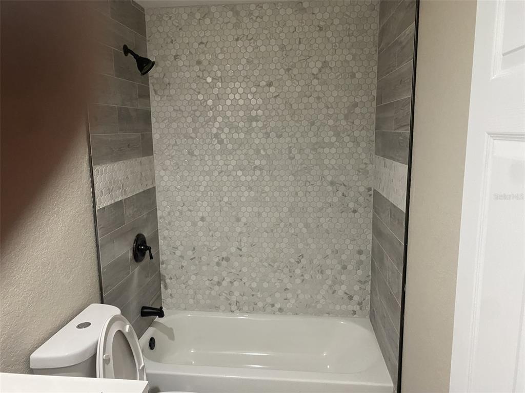 A bathroom features a white bathtub with a gray wood-look tile and hexagon tile surround — 1938 SW DUKE STREET, ARCADIA, FL