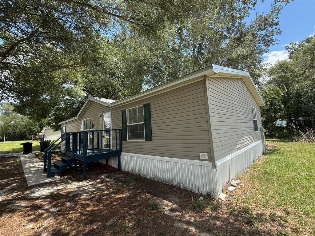 A tan manufactured home with white skirting and a blue wooden deck under large trees — 17199 SE 97TH TERRACE, SUMMERFIELD, FL