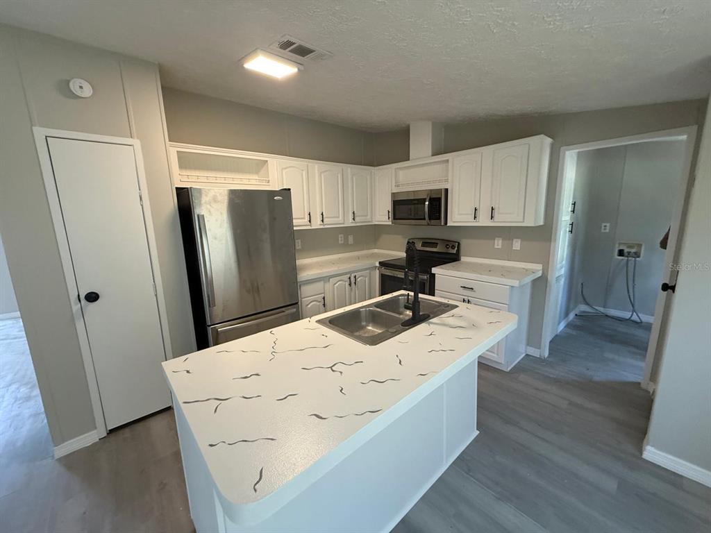 A kitchen features white cabinets, stainless steel appliances, and a central island with marble-patterned countertops — 17199 SE 97TH TERRACE, SUMMERFIELD, FL