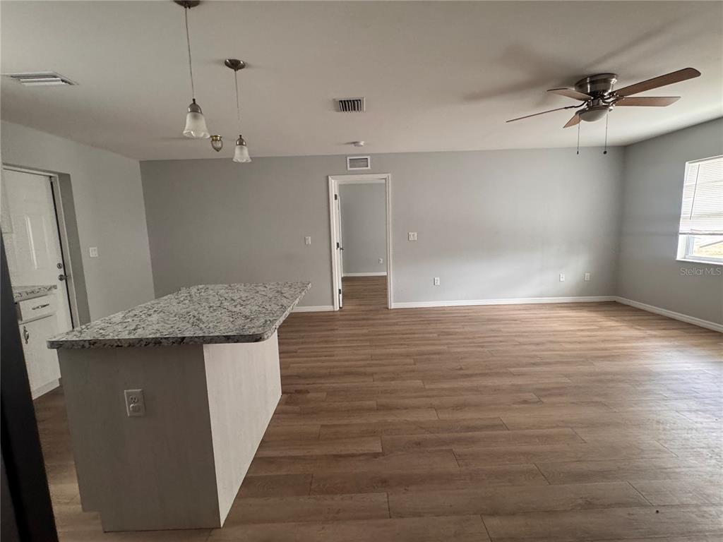 An open-concept living area features wood-look flooring, a granite-topped kitchen island, and a ceiling fan — 625 N THIRTEENTH AVENUE, ARCADIA, FL