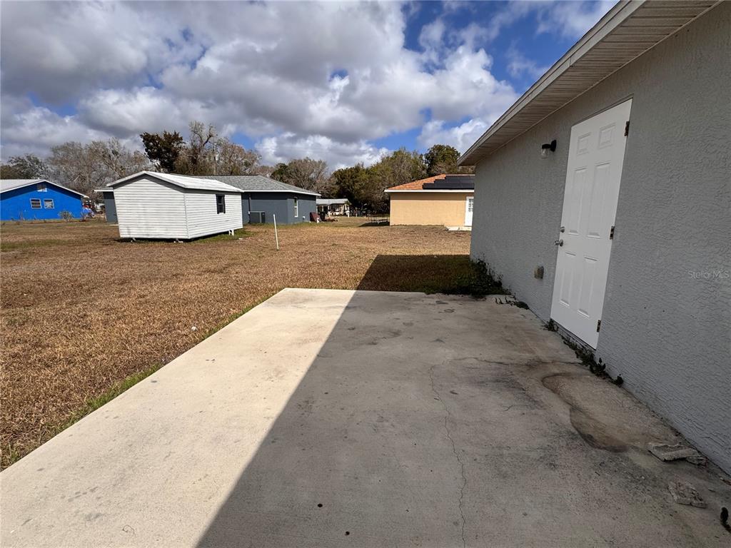 A concrete patio sits outside a gray house with a white door and a shed — 625 N THIRTEENTH AVENUE, ARCADIA, FL