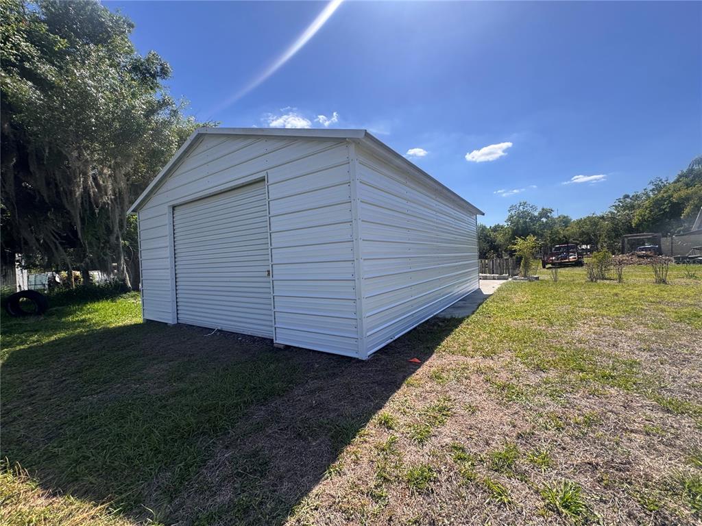 A white metal storage shed with a roll-up door sits on a grassy lot — 625 N THIRTEENTH AVENUE, ARCADIA, FL