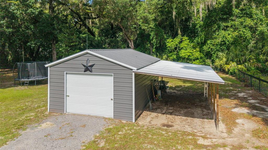 A gray metal garage with a white roll-up door and an attached open-sided carport — 14366 NE 42ND TERRACE, ANTHONY, FL