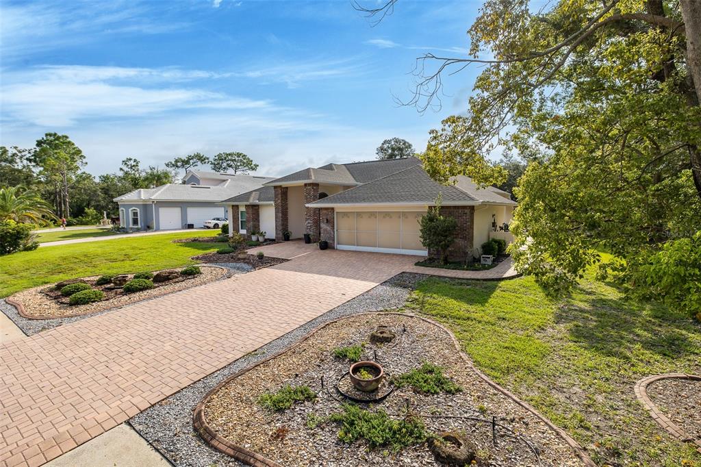 A single-story house with a brick facade, a paved driveway, and landscaped garden beds — 18822 MAJESTIC OAK COURT, HUDSON, FL