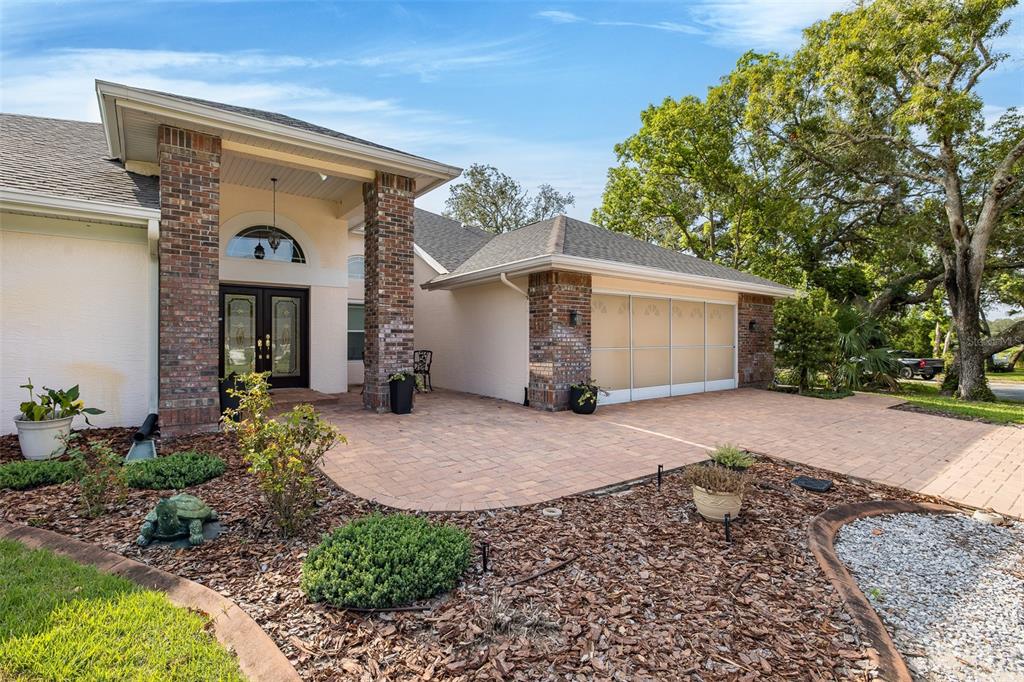 A brick-columned entryway leads to a front door and a garage with translucent panels — 18822 MAJESTIC OAK COURT, HUDSON, FL