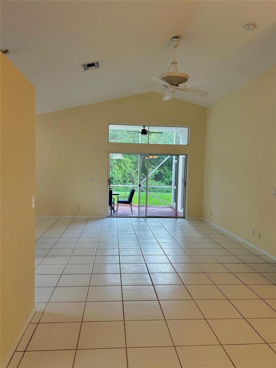 A spacious living room with light-colored tile flooring, vaulted ceilings, and sliding glass patio doors — 3694 Miramontes Circle, Wellington FL 33414, WELLINGTON, FL