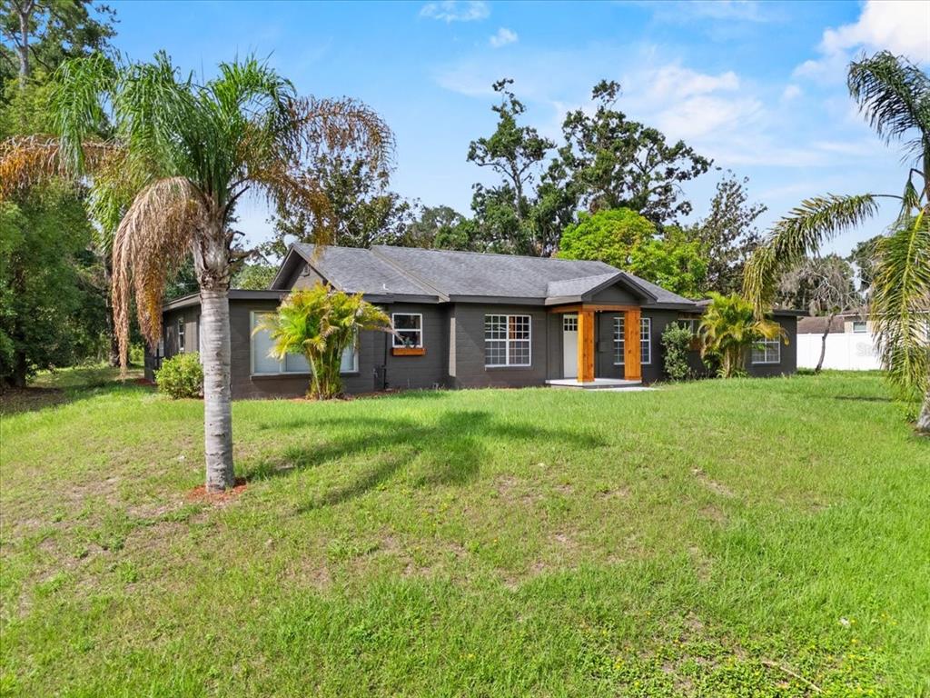 A single-story house with dark gray exterior walls, a gabled entryway, and surrounding palm trees — 504 PRADO PLACE, LAKELAND, FL