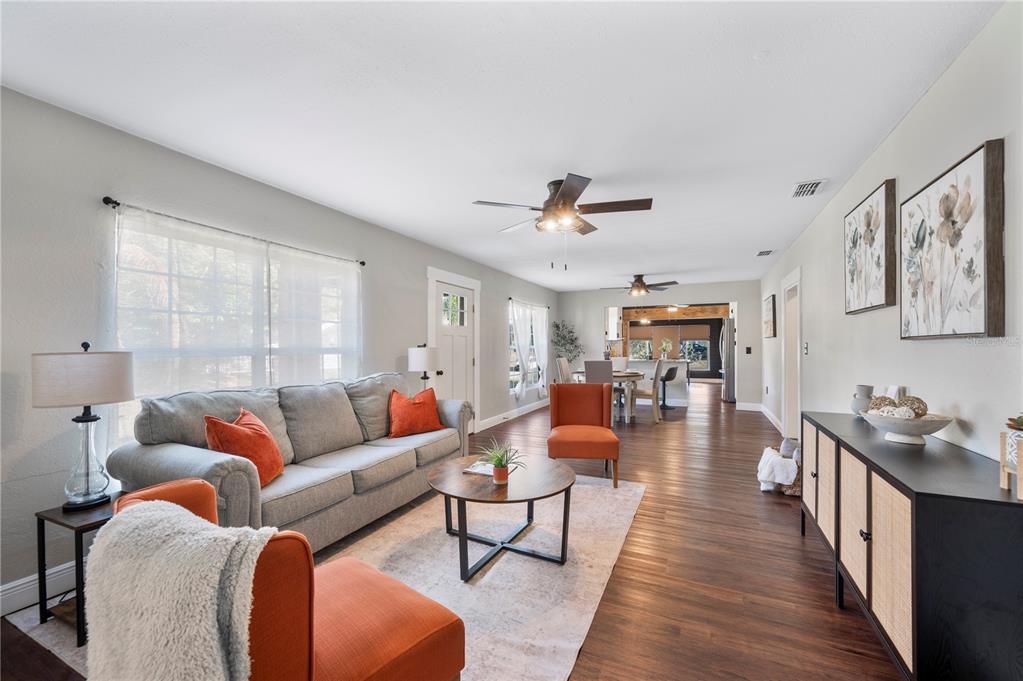 A living room with gray sofa, orange accent chairs, wood floors, and an open dining area — 504 PRADO PLACE, LAKELAND, FL