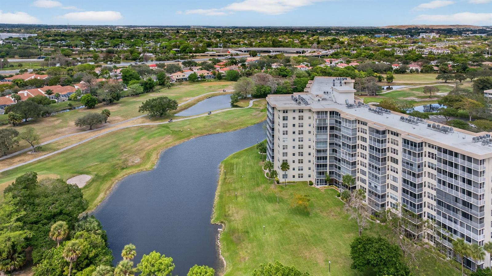 An aerial view shows a multi-story apartment building situated next to a golf course pond — 3507 Oaks Way # 501, Pompano Beach FL 33069, POMPANO BEACH, FL