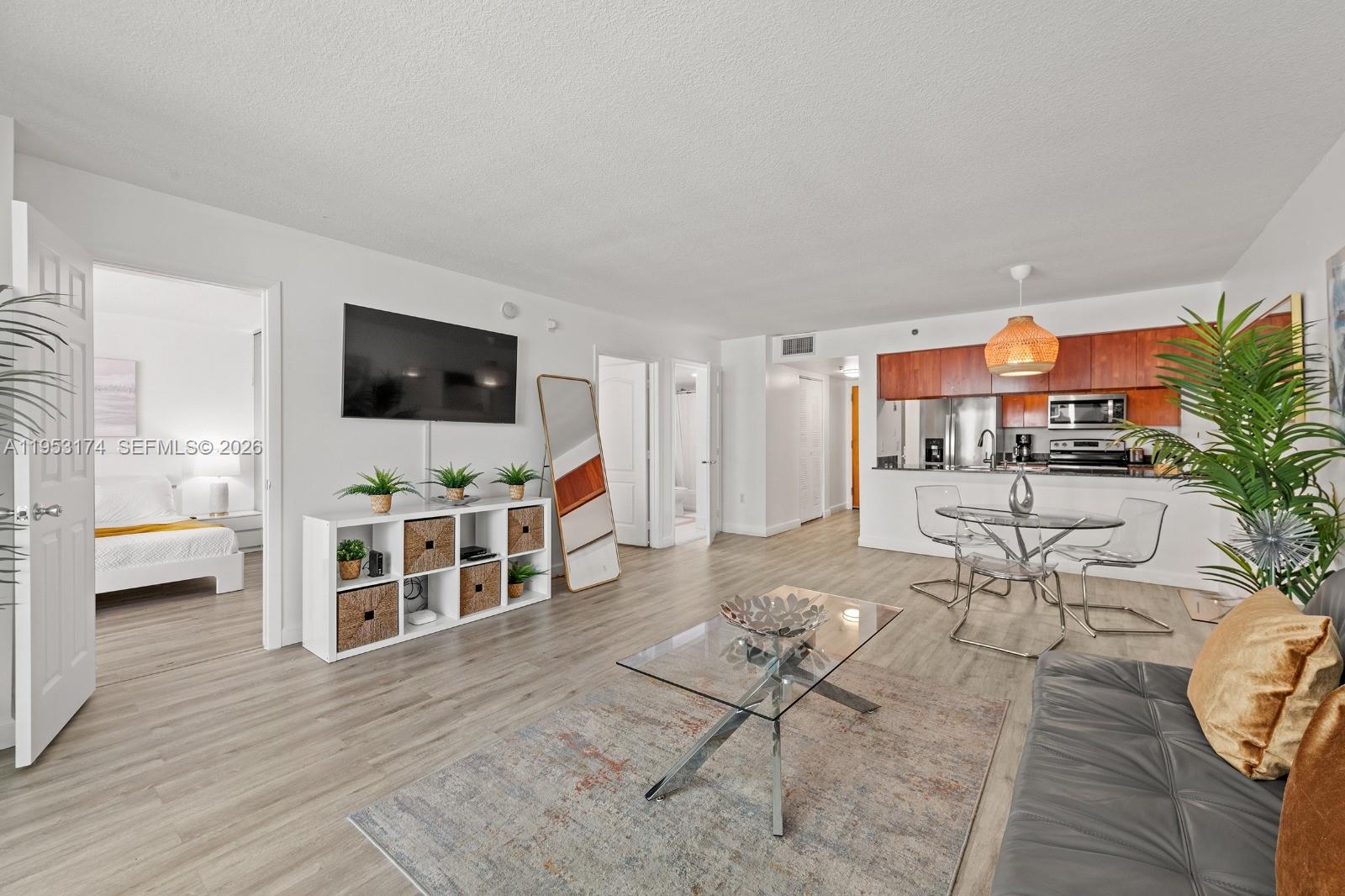 An open-concept living and dining area features wood-look flooring, a glass coffee table, and kitchen — 1200 Brickell Bay Dr # 2414, Miami FL 33131, MIAMI, FL