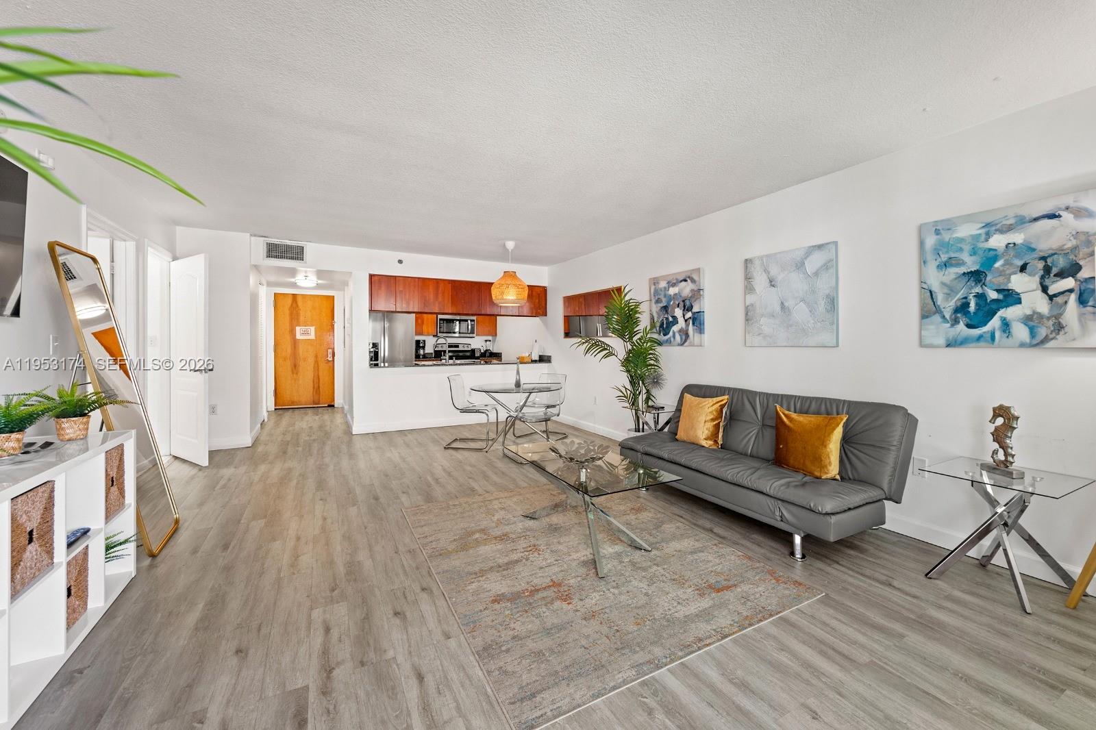 A living room with wood-look flooring, a grey sofa, and an open kitchen area — 1200 Brickell Bay Dr # 2414, Miami FL 33131, MIAMI, FL