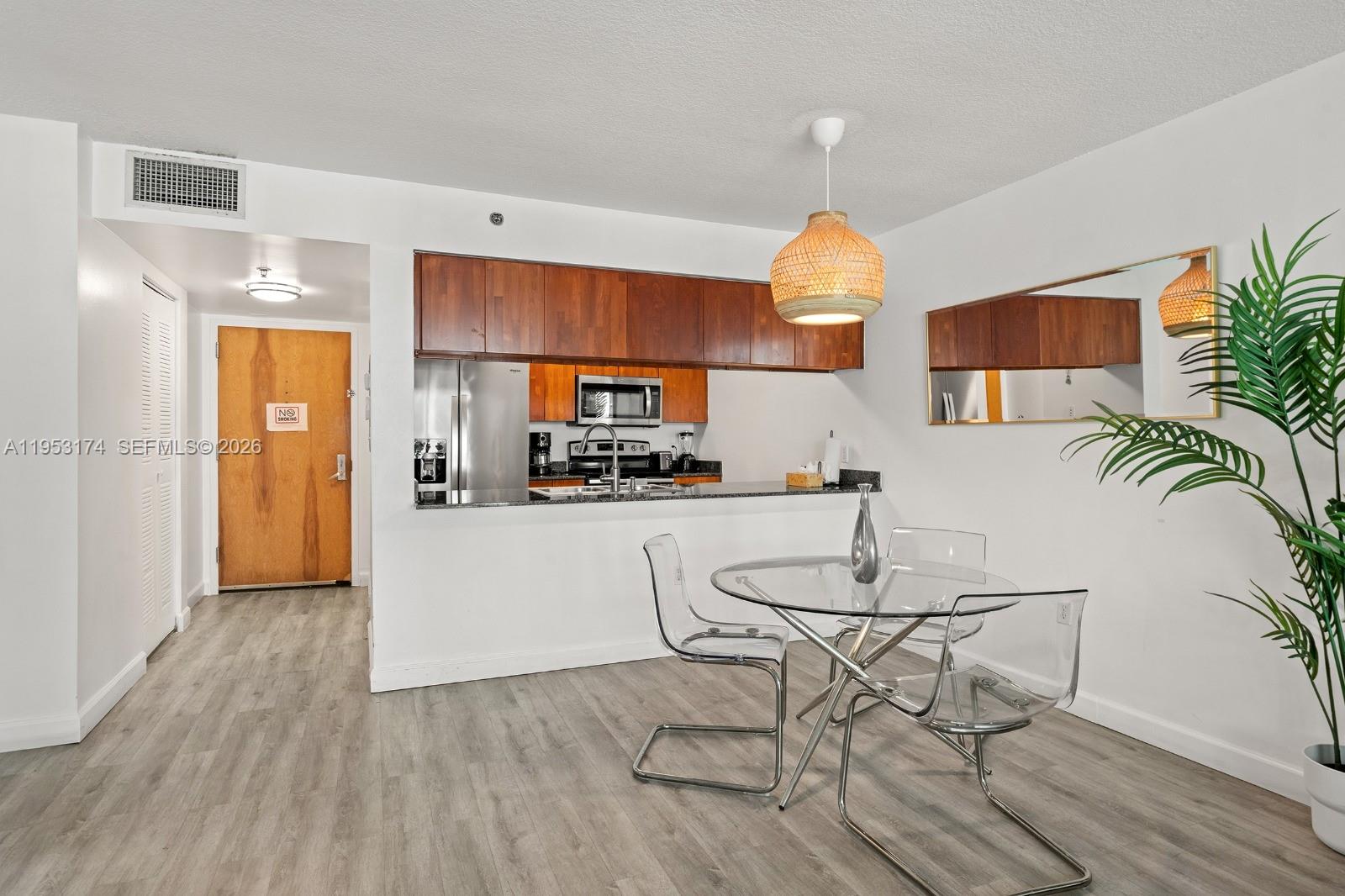 A dining area with a glass table and clear chairs sits before an open kitchen — 1200 Brickell Bay Dr # 2414, Miami FL 33131, MIAMI, FL
