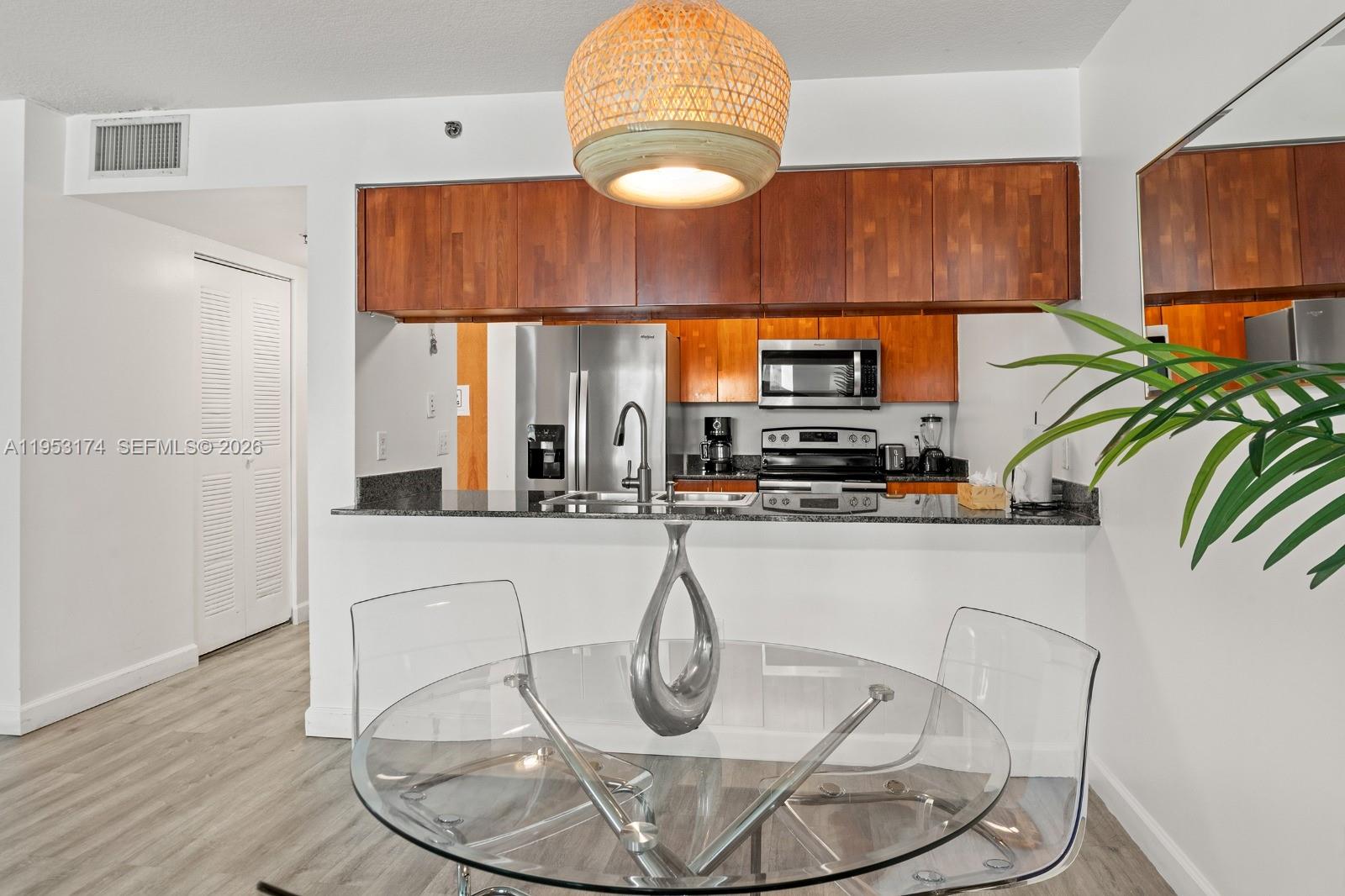 A kitchen with wood cabinets and stainless steel appliances overlooks a dining area with chairs — 1200 Brickell Bay Dr # 2414, Miami FL 33131, MIAMI, FL