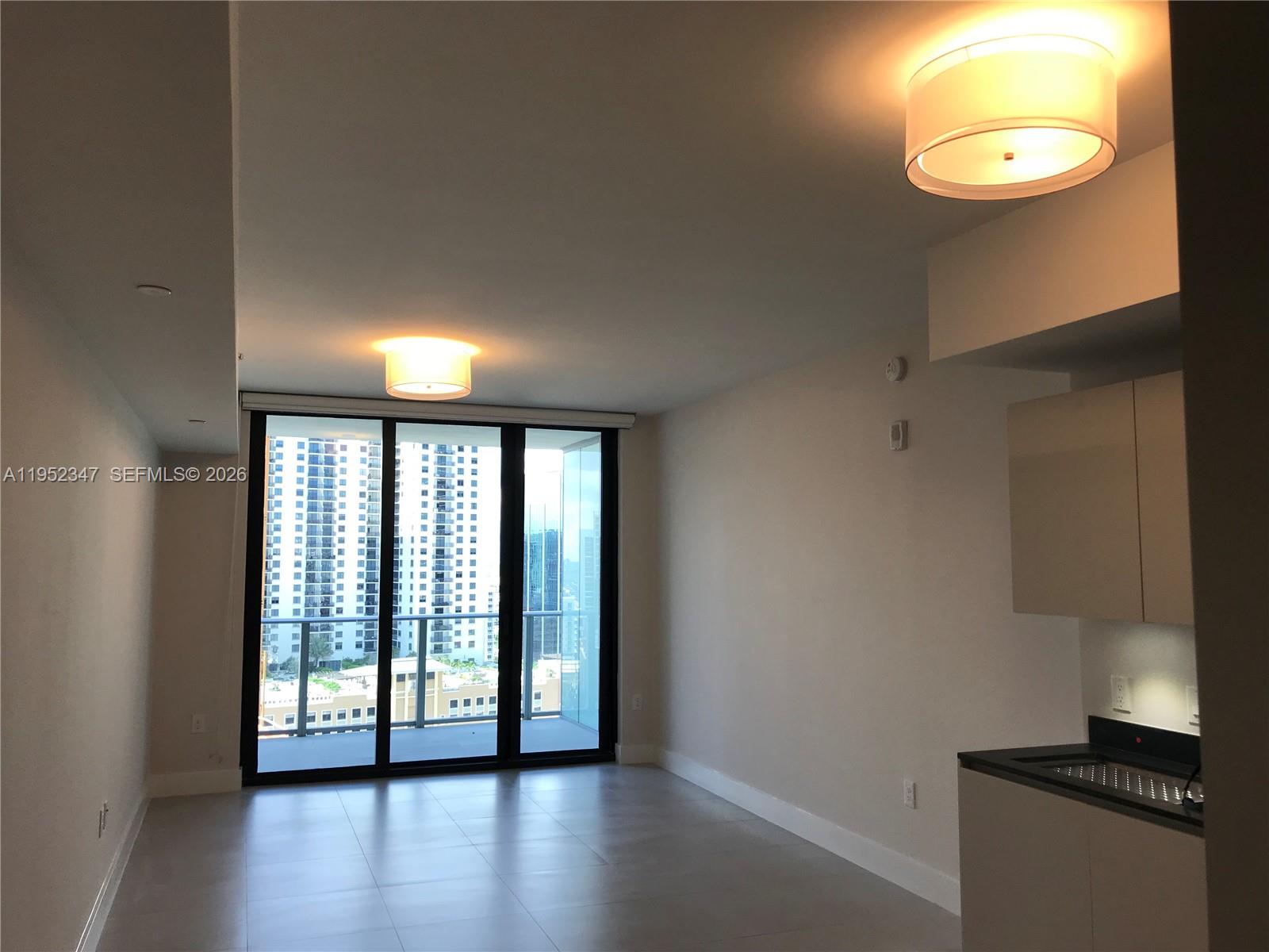 An unfurnished living area features light tile flooring, two ceiling lights, and floor-to-ceiling balcony doors — 1010 BRICKELL AVE # 2110, Miami FL 33131, MIAMI, FL