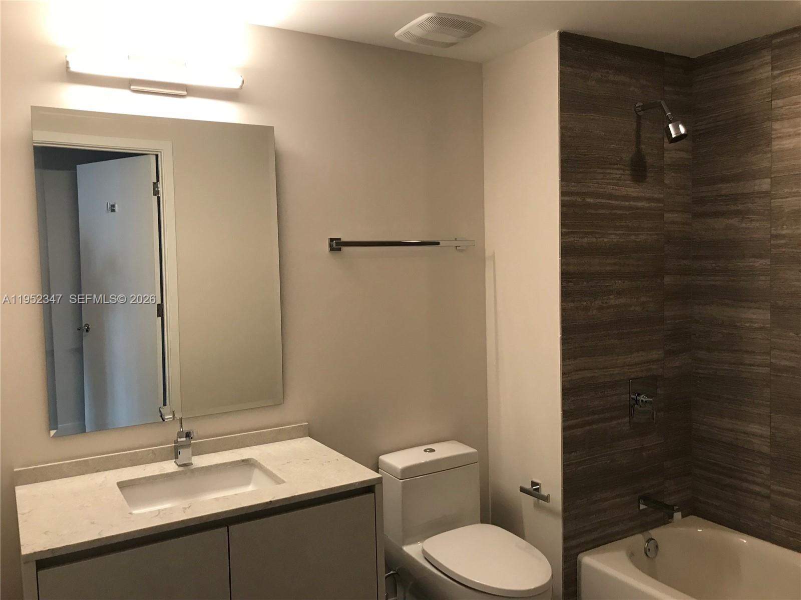 A modern bathroom features a vanity, toilet, and a shower-tub combo with wood-look tile — 1010 BRICKELL AVE # 2110, Miami FL 33131, MIAMI, FL