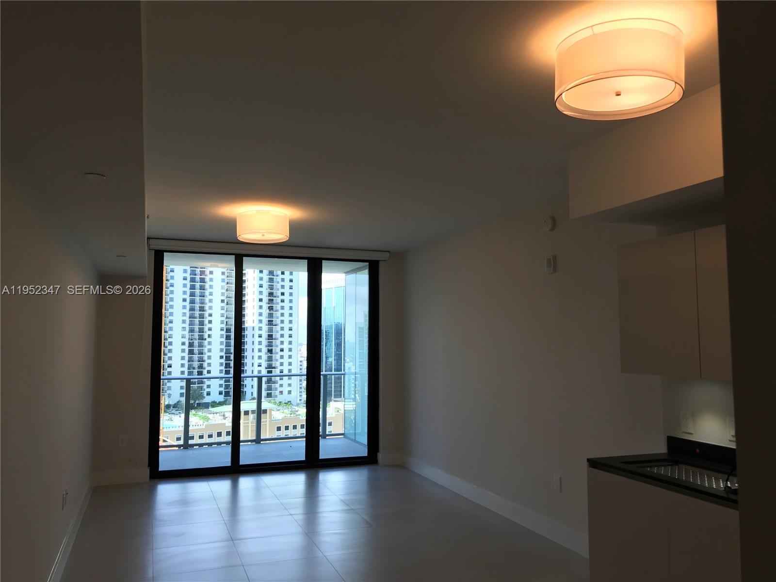 An empty room with light-colored tile floors, two ceiling light fixtures, and a balcony view — 1010 BRICKELL AVE # 2110, Miami FL 33131, MIAMI, FL